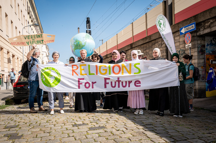 Ein Banner mit der Aufschrift Religions For Future wird vor einem Demonstrationszug gehalten.)