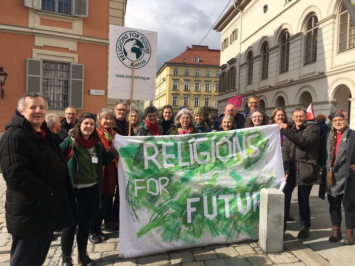 Menschen mit einem Religions For Future Banner auf einem Platz.