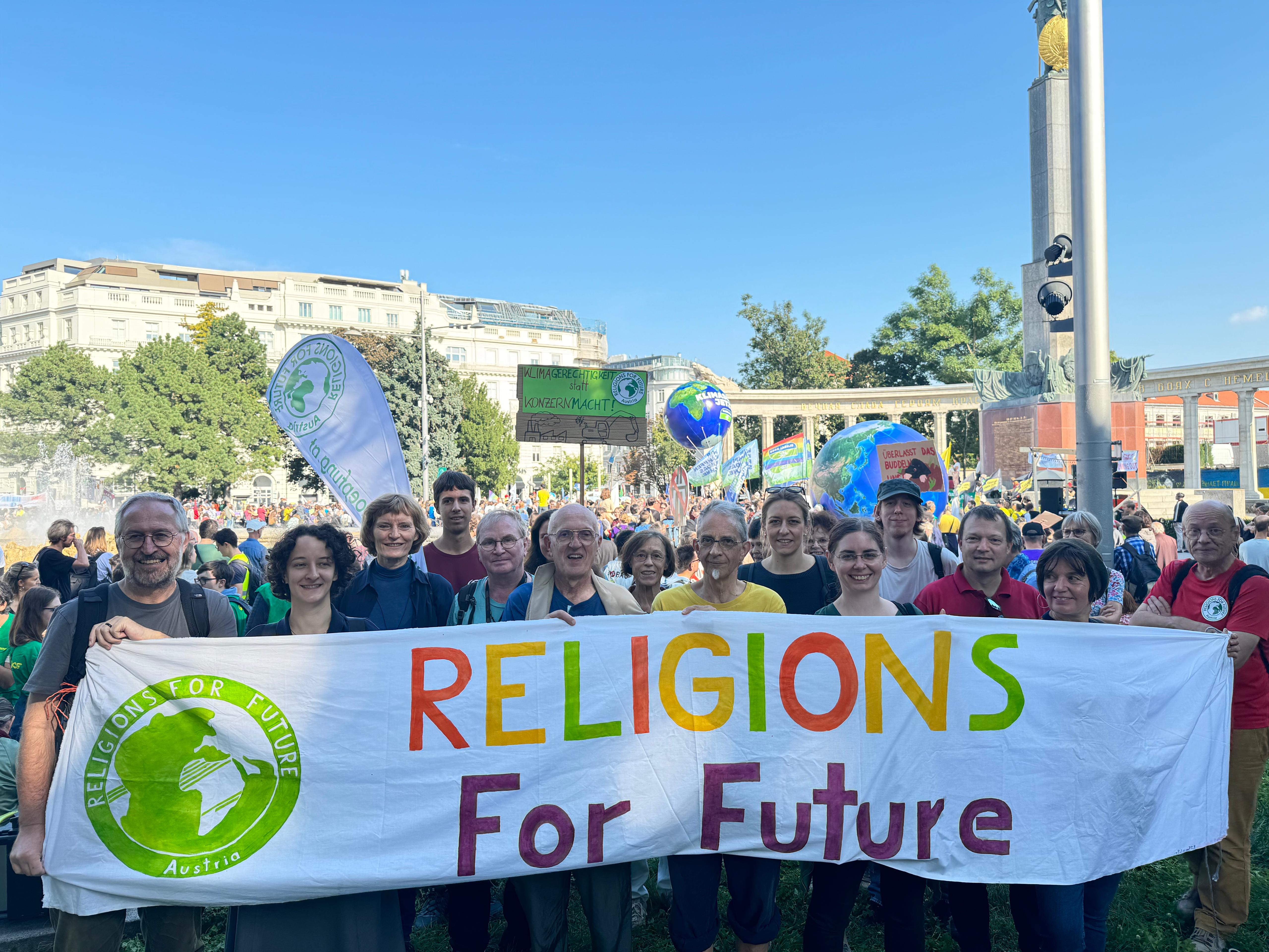 Ein Banner mit der Aufschrift Religions For Future wird vor einem Demonstrationszug gehalten.)